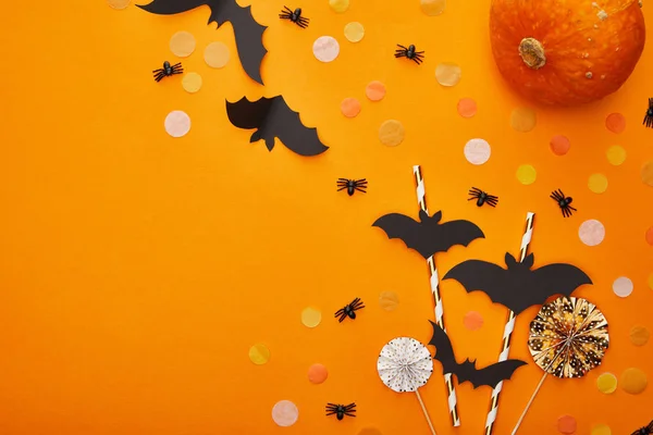 Vue de dessus de citrouille, chauves-souris et araignées avec confettis sur fond orange, décoration d'Halloween — Photo de stock