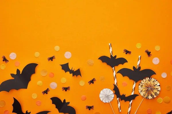 Vista superior de murciélagos y arañas con confeti sobre fondo naranja, decoración de Halloween - foto de stock