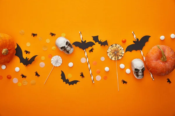 Top view of pumpkin, skulls, bats and spiders with confetti on orange background, Halloween decoration — Stock Photo