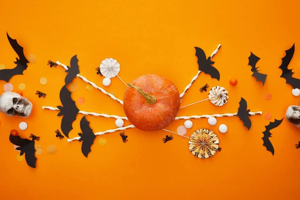 Top view of pumpkin, skulls, bats and spiders with confetti on orange background, Halloween decoration — Stock Photo