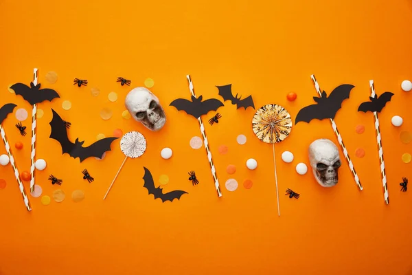 Vista superior de cráneos, murciélagos y arañas con confeti sobre fondo naranja, decoración de Halloween - foto de stock