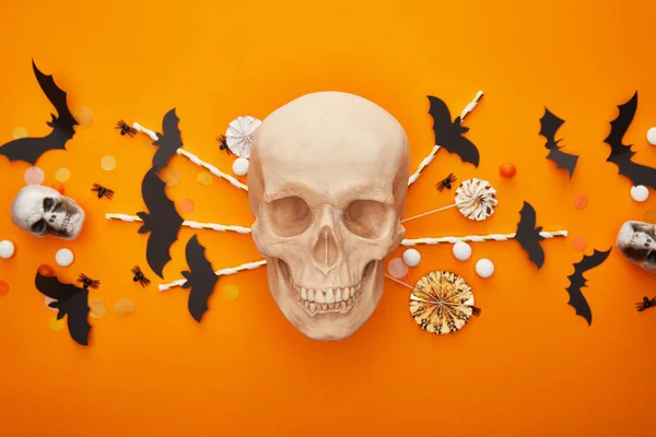 Vista superior del cráneo con murciélagos y arañas y confeti sobre fondo naranja, decoración de Halloween - foto de stock