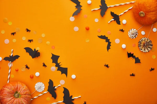 Top view of pumpkin, bats and spiders with confetti on orange background, Halloween decoration — Stock Photo