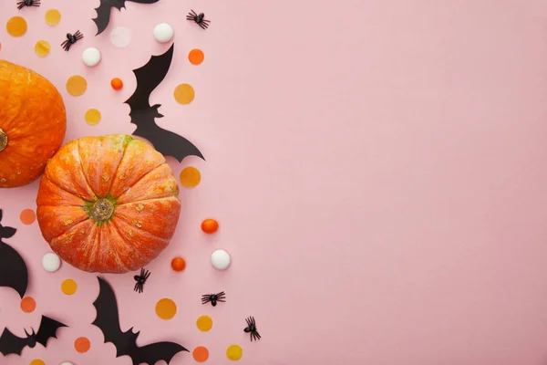 Vue de dessus de citrouille, chauves-souris et araignées avec confettis sur fond rose, décoration d'Halloween — Photo de stock