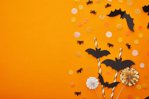 Vista superior de murciélagos y arañas con confeti sobre fondo naranja, decoración de Halloween - foto de stock