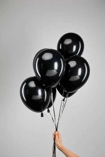 Visión parcial de la mujer sosteniendo racimo de globos negros aislados en gris, concepto de viernes negro - foto de stock