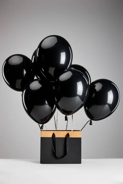Bunch of black balloons with paper shopping bag isolated on grey, black Friday concept — Stock Photo