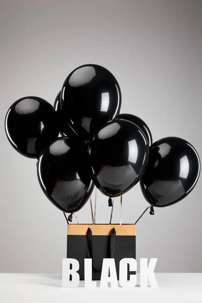 Bunch of black balloons with paper shopping bag isolated on grey, black Friday concept — Stock Photo