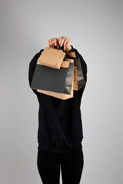 Жінка з незрозумілим обличчям тримає паперові сумки ізольовані на сірій, чорній концепції п'ятниці — стокове фото