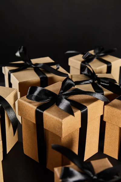 Selective focus of cardboard gift boxes with black ribbons isolated on black, black Friday concept — Stock Photo