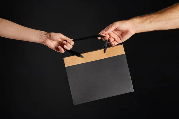 Vista recortada de la mujer y el hombre sosteniendo bolsa de compras de papel aislado en negro, concepto de viernes negro - foto de stock