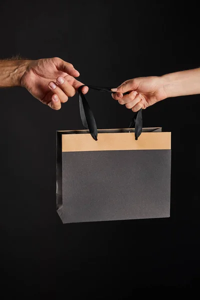 Cropped view of woman and man holding paper shopping bag isolated on black, black Friday concept — Stock Photo