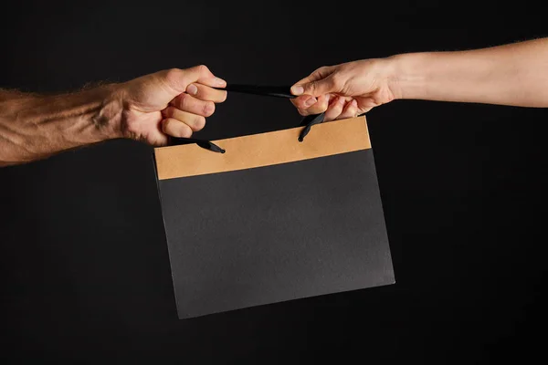 Partial view of woman and man holding paper shopping bag isolated on black, black Friday concept — Stock Photo