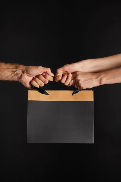 Partial view of woman and man holding paper shopping bag isolated on black, black Friday concept — Stock Photo