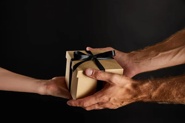 Vista recortada de hombre y mujer sosteniendo caja de regalo de cartón con cinta aislada en negro, concepto de viernes negro - foto de stock