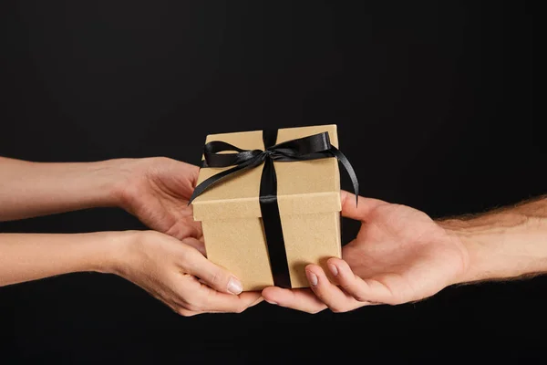 Обрізаний вид чоловіка і жінки, що тримає картонну подарункову коробку зі стрічкою ізольовано на чорній, чорній концепції п'ятниці — стокове фото