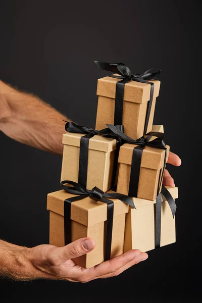 Обрізаний вид людини, що тримає картонні подарункові коробки зі стрічками ізольовані на чорній, чорній концепції п'ятниці — стокове фото