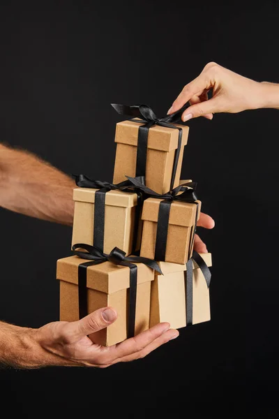 Обрізаний вид чоловіка і жінки, що тримає картонні подарункові коробки зі стрічками ізольовані на чорній, чорній концепції п'ятниці — стокове фото