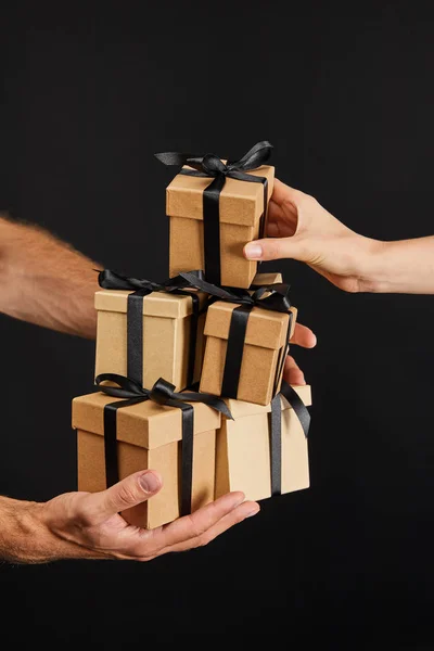 Vista recortada de hombre y mujer sosteniendo cajas de regalo de cartón con cintas aisladas en negro, concepto de viernes negro - foto de stock