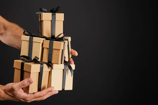 Abgeschnittene Ansicht eines Mannes mit Geschenkkartons aus Pappe mit Schleifen, isoliert auf schwarzem, schwarzem Freitag-Konzept — Stockfoto