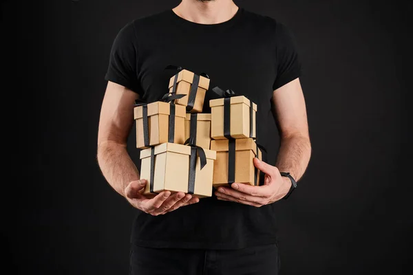 Vista recortada del hombre sosteniendo cajas de regalo de cartón con cintas aisladas en negro, concepto de viernes negro - foto de stock