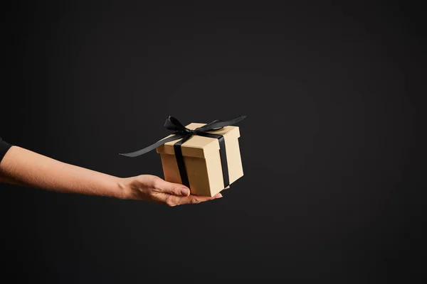 Обрізаний вид жінки, що тримає картонну подарункову коробку зі стрічкою ізольовано на чорній, чорній концепції п'ятниці — стокове фото