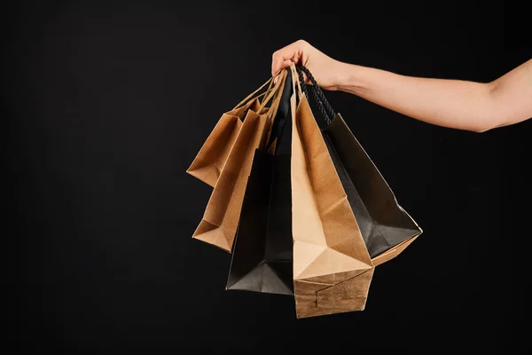 Vista parcial de la mujer sosteniendo bolsas de compras de papel aislado en negro, concepto de viernes negro - foto de stock