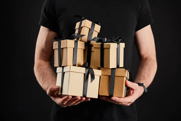 Partial view of man holding cardboard gift boxes with ribbons isolated on black, black Friday concept — Stock Photo