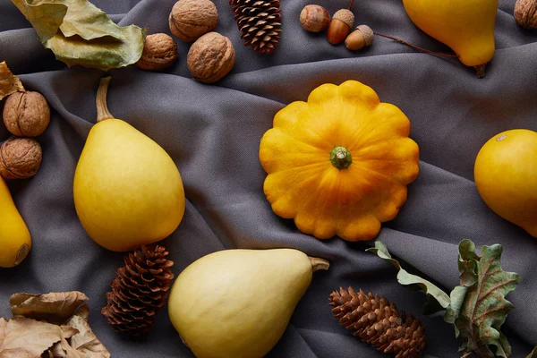 Спелые целые красочные тыквы, орехи и шишки на серой ткани — стоковое фото