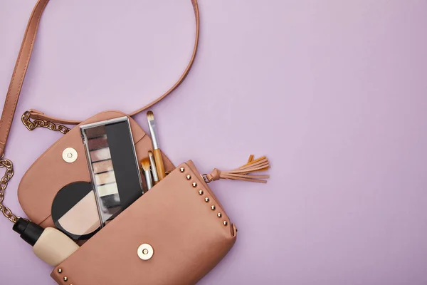 Vista dall'alto di cosmetici decorativi e pennelli per il trucco in borsa isolati su viola — Foto stock