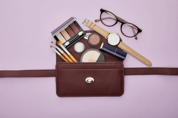 Top view of decorative cosmetics near watch and glasses isolated on violet — Stock Photo