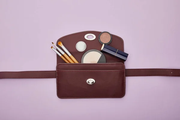 Top view of decorative cosmetics near bag isolated on violet — Stock Photo