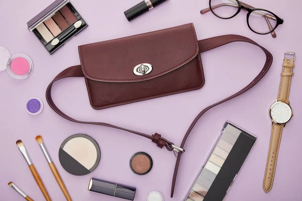 Draufsicht der Tasche in der Nähe von dekorativer Kosmetik isoliert auf violett — Stockfoto