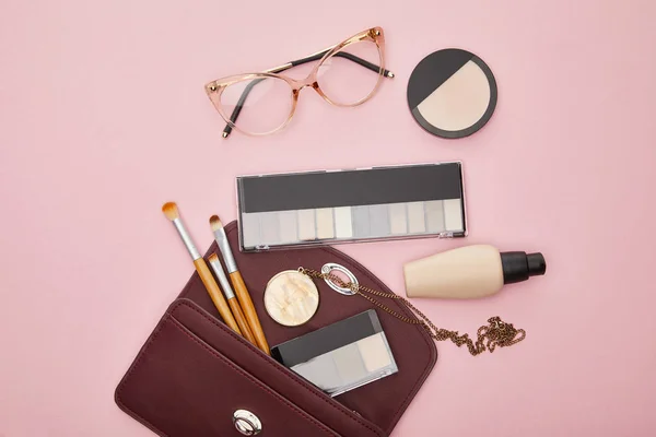 Vista superior de óculos perto do saco com cosméticos decorativos isolados em rosa — Fotografia de Stock