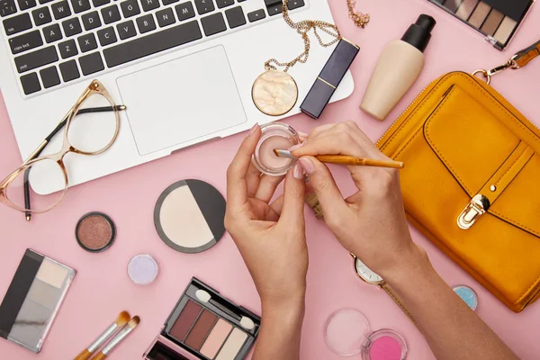 Vista recortada de la mujer sosteniendo cepillo cosmético cerca de corrector aislado en rosa - foto de stock