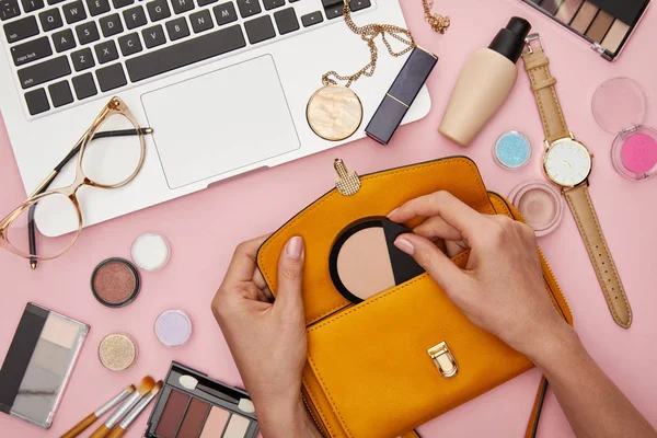 Vista recortada de la mujer que sostiene el bolso cerca de cosméticos decorativos aislados en rosa - foto de stock