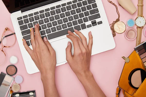 Vista superior da mulher digitando no laptop perto de cosméticos decorativos e colar isolado em rosa — Fotografia de Stock