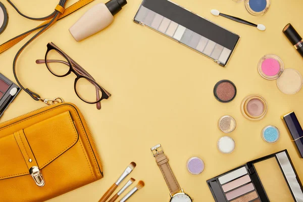 Vista dall'alto della borsa vicino cosmetici decorativi e occhiali isolati su giallo — Foto stock