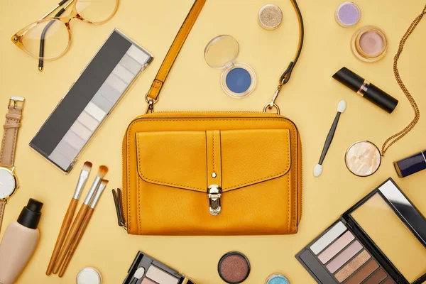 Top view of bag near decorative cosmetics and necklace isolated on yellow — Stock Photo