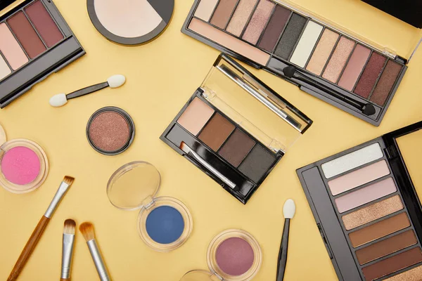 Top view of set with brown eye shadow near cosmetic brushes isolated on yellow — Stock Photo