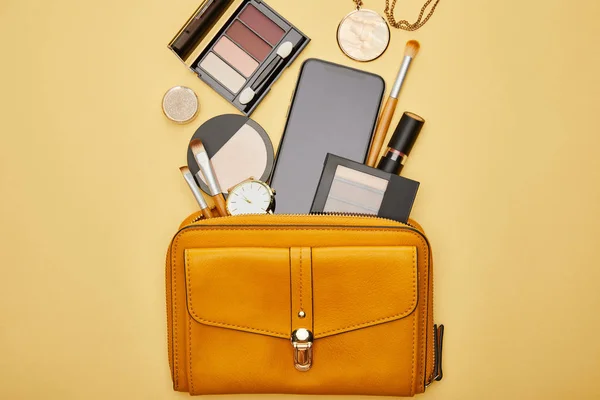Vista superior de la bolsa con smartphone y cosméticos decorativos aislados en amarillo - foto de stock