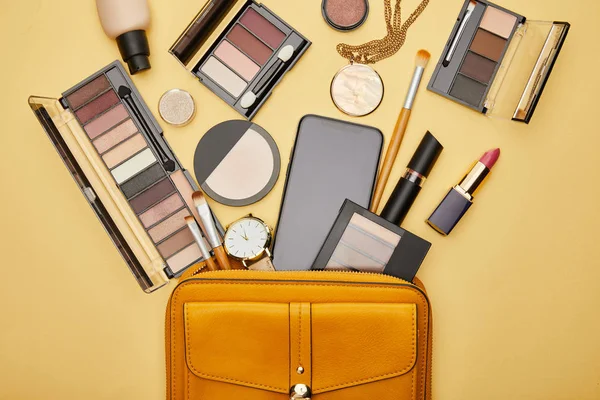 Vista superior do saco com cosméticos decorativos e smartphone com tela em branco isolado no amarelo — Fotografia de Stock