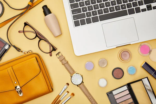 Vista superior de la computadora portátil cerca de gafas y cosméticos decorativos aislados en amarillo - foto de stock