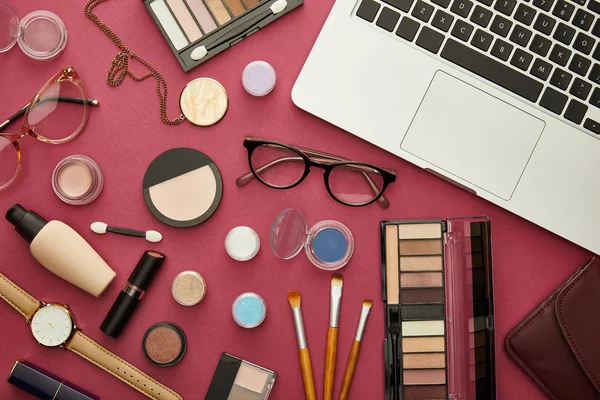 Top view of laptop near decorative cosmetics and glasses on crimson — Stock Photo