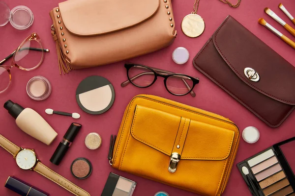 Top view of stylish bags near decorative cosmetics isolated on crimson — Stock Photo