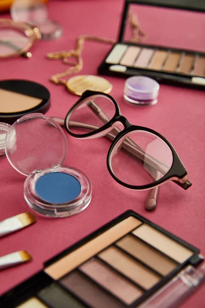 Foyer sélectif de lunettes près de cosmétiques décoratifs sur cramoisi — Photo de stock