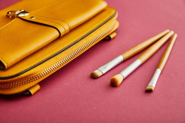 Close up of cosmetic brushes near yellow bag on crimson — Stock Photo