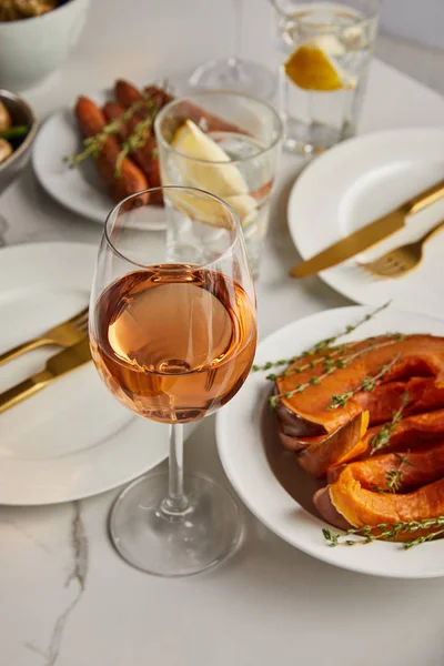 Selective focus of glass with rose wine near baked sliced pumpkin of marble table — Stock Photo