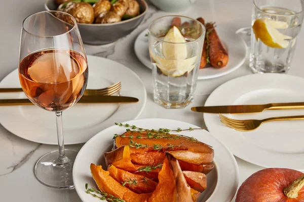 Zucca al forno e bicchieri con acqua al limone e vino rosato sul tavolo di marmo — Foto stock