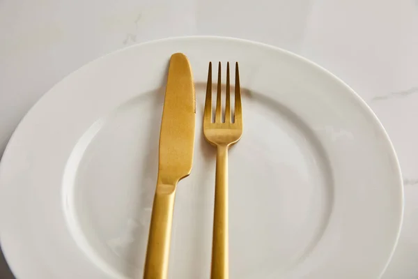 Faca dourada e garfo na placa branca limpa na mesa de mármore — Fotografia de Stock